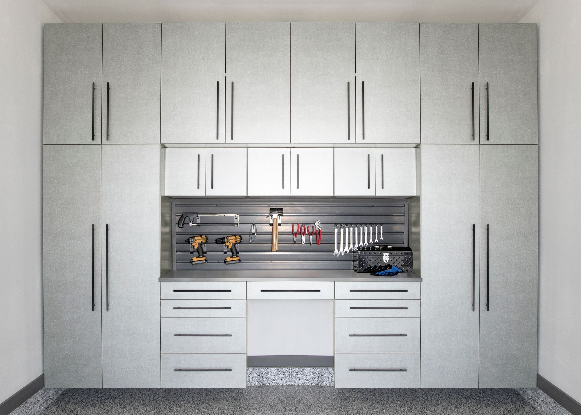 Built-in gray garage wall with storage cabinets, central workbench, tools, and lower drawers