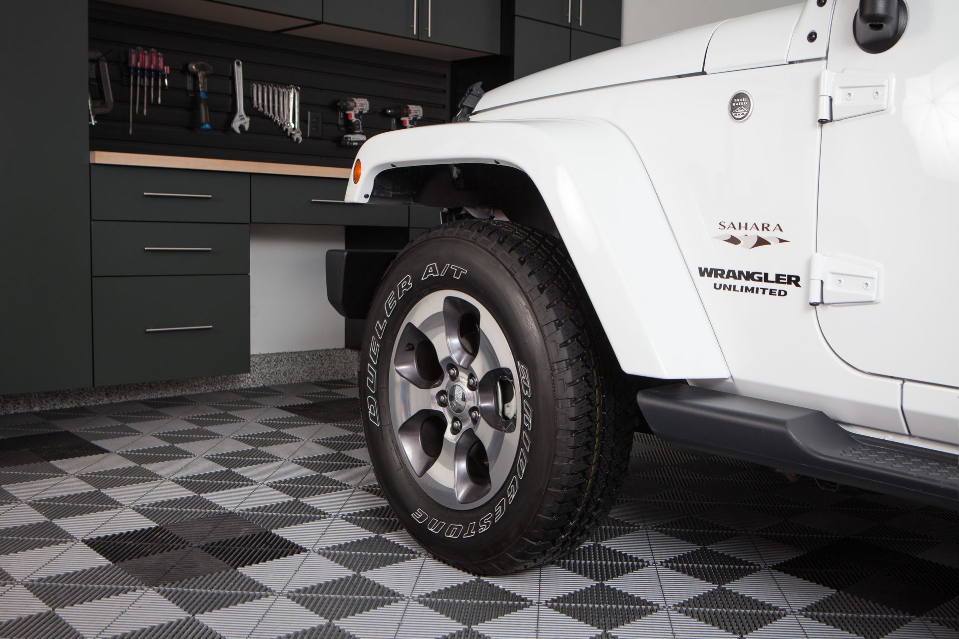 White Jeep parked in a garage beside dark green cabinets on a checkered floor