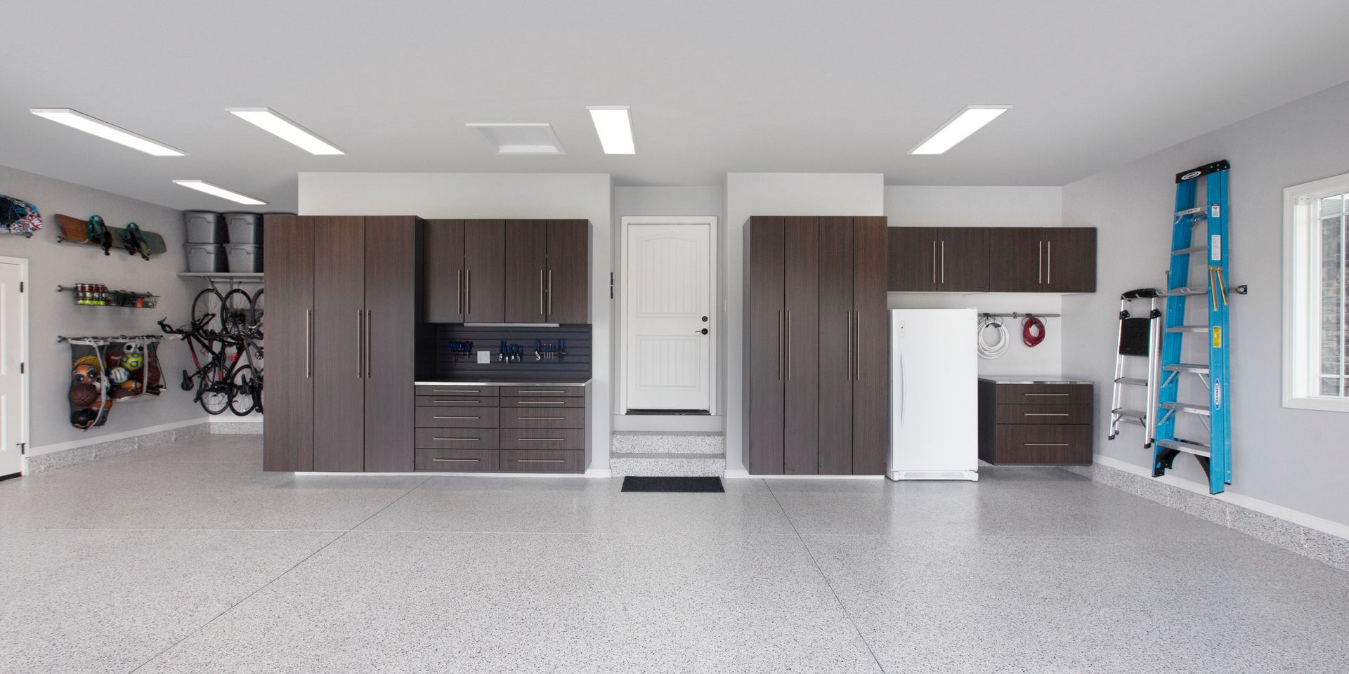 Empty garage with gray cabinets, workbench, white door, and blue ladder on the right wall