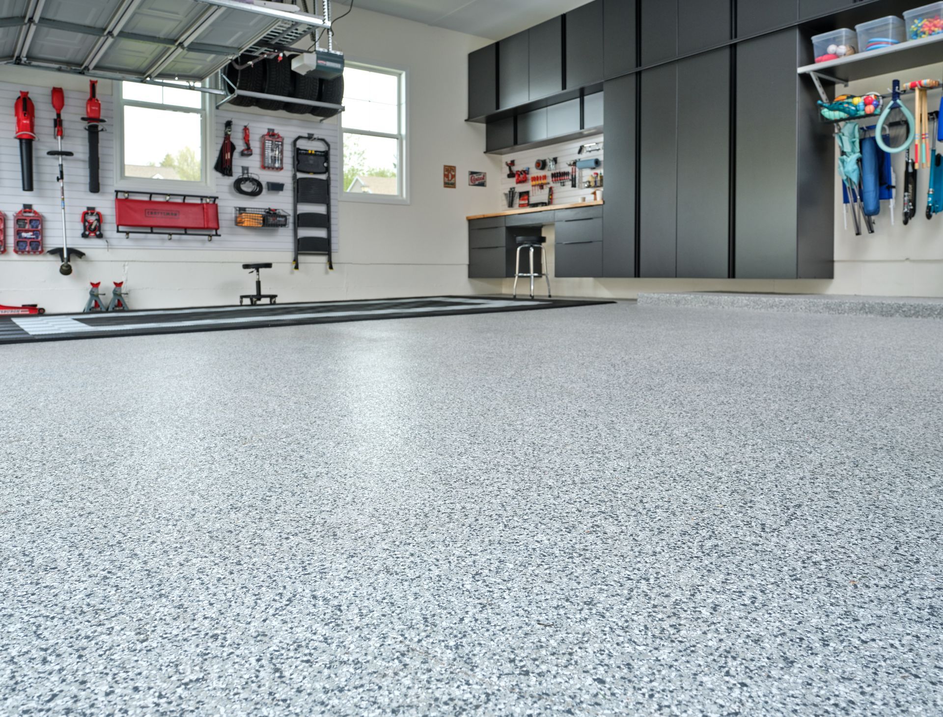 A clean garage with gray epoxy floor, wall cabinets, tools, and bikes hanging on the right.