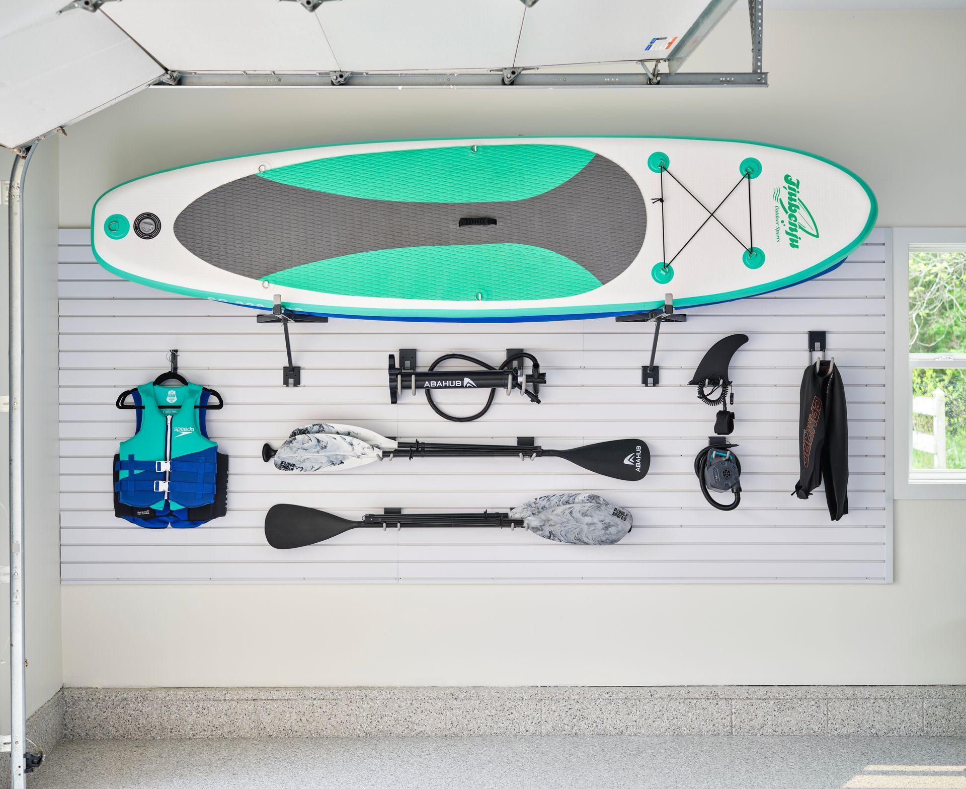 Surfboard and water sports gear hung on a garage wall rack.