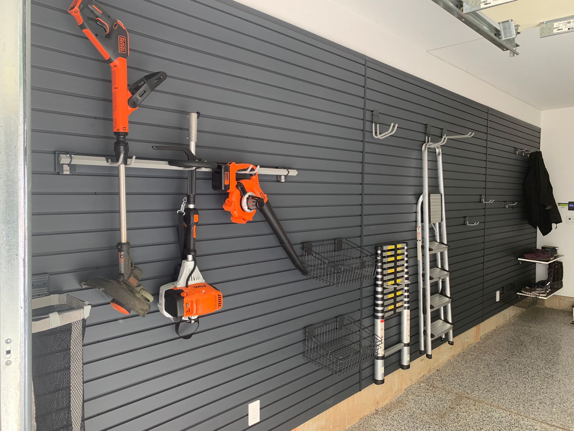 Garage wall with orange power tools, ladders, and equipment mounted on a dark slatwall display.
