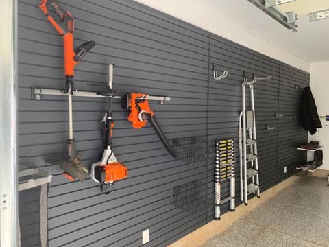 Wall-mounted garden tools and ladders displayed on a gray slatwall in a garage showroom
