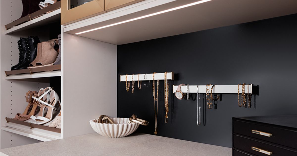 Built-in closet organizer with shelves, hanging jewelry, and a white decorative bowl on a dark background