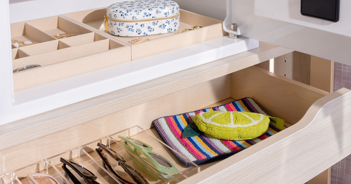 Open kitchen drawer with cutlery and colorful woven placemats organized in a tray.