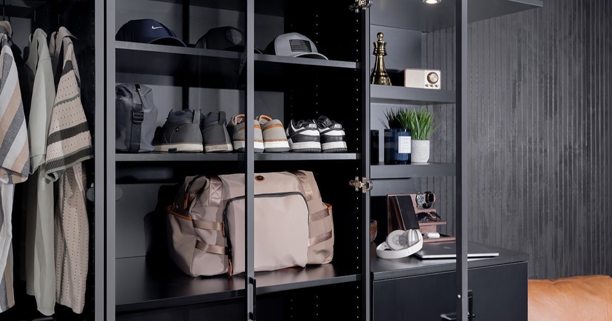 Open closet with shelves of clothes, shoes, bags, and a striped shirt beside gray sliding doors.