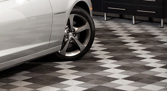 Silver car parked on a black-and-white checkered garage floor near dark cabinets