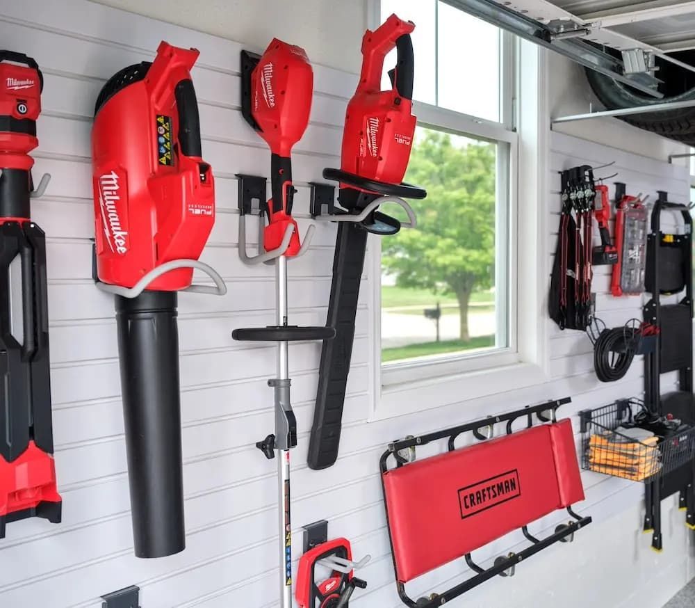 Red Milwaukee and Craftsman tools organized on a white garage wall near a window.