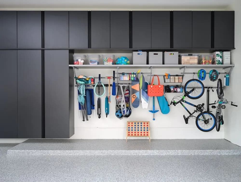 Garage wall with black cabinets, shelves, and hanging bikes, tools, and sports gear organized on hooks.