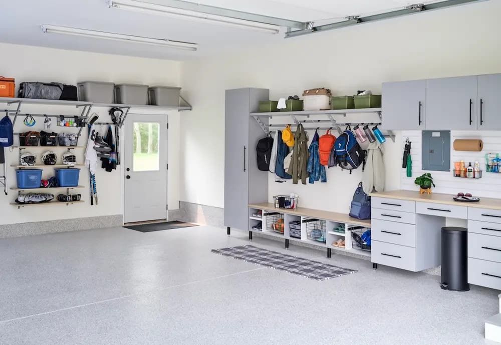 Bright garage with organized tools, cabinets, hanging jackets, workbench, and white walls and floor.