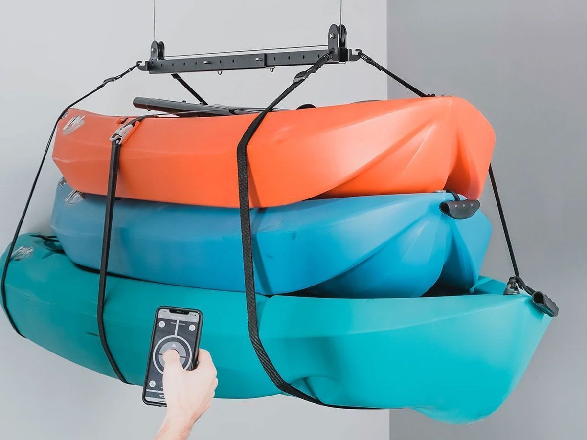 Stacked colorful inflatable kayaks with straps, being compressed by a handheld remote-controlled lifting device.
