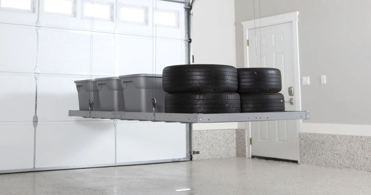 Tires stored on a metal shelf in a garage beside white cabinets and a speckled floor
