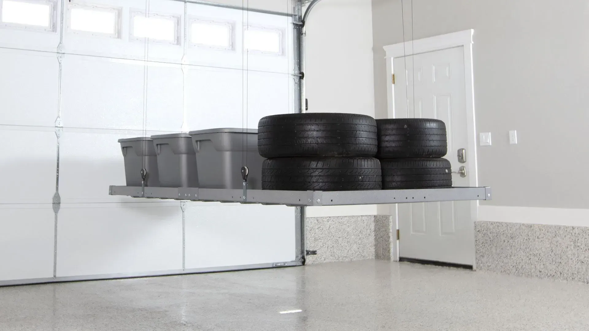 Garage with a trailer carrying stacked black tires and gray bins, parked in front of a white garage door