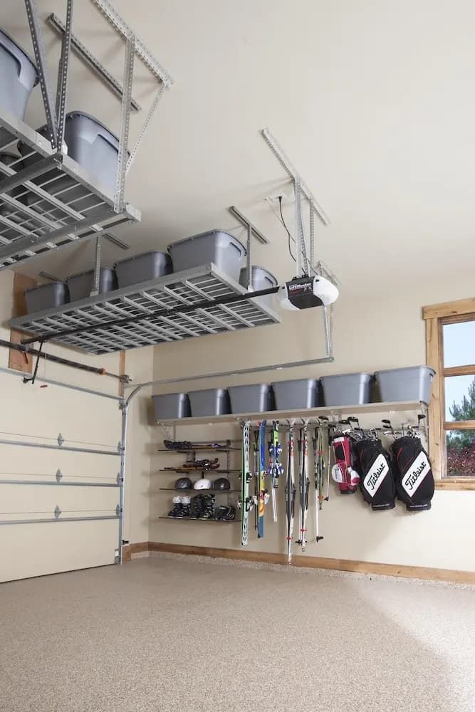 Garage with overhead storage racks, hanging tools, shelves, and mounted ski equipment on a beige wall.