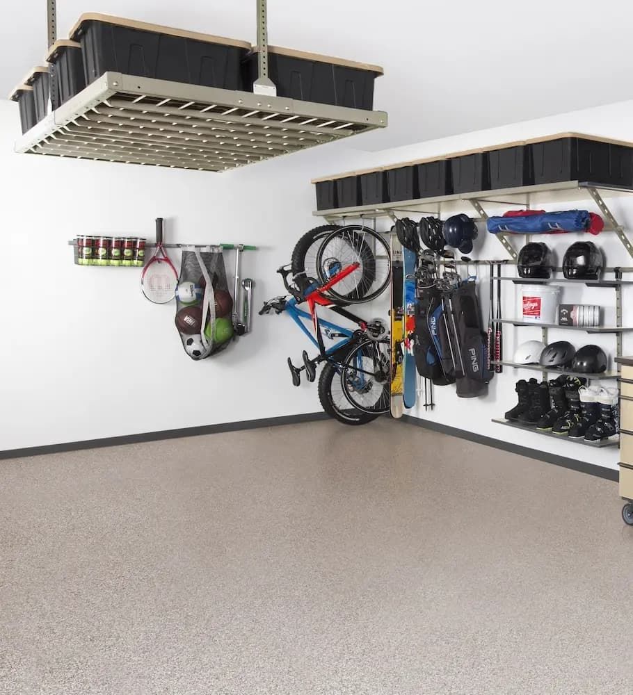 Garage with wall-mounted storage racks holding bikes, helmets, sports gear, and shoes under a ceiling storage platform