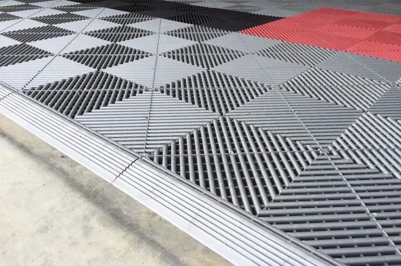 Gray and black diamond-pattern floor mats with a red section on a concrete surface