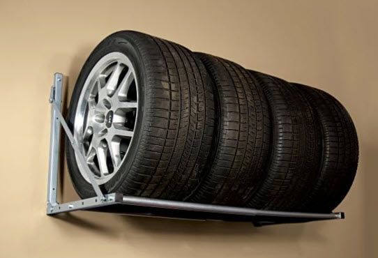 Wall-mounted tire rack holding three black tires and a silver wheel against a beige wall
