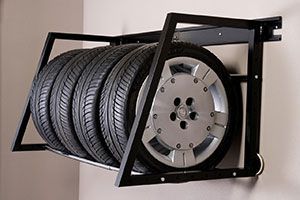 Wall-mounted rack holding stacked tires and a silver car wheel rim