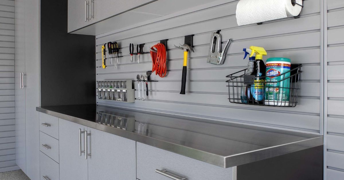 Gray garage workbench with slatwall organizer, hanging tools, and cleaning supplies above cabinets