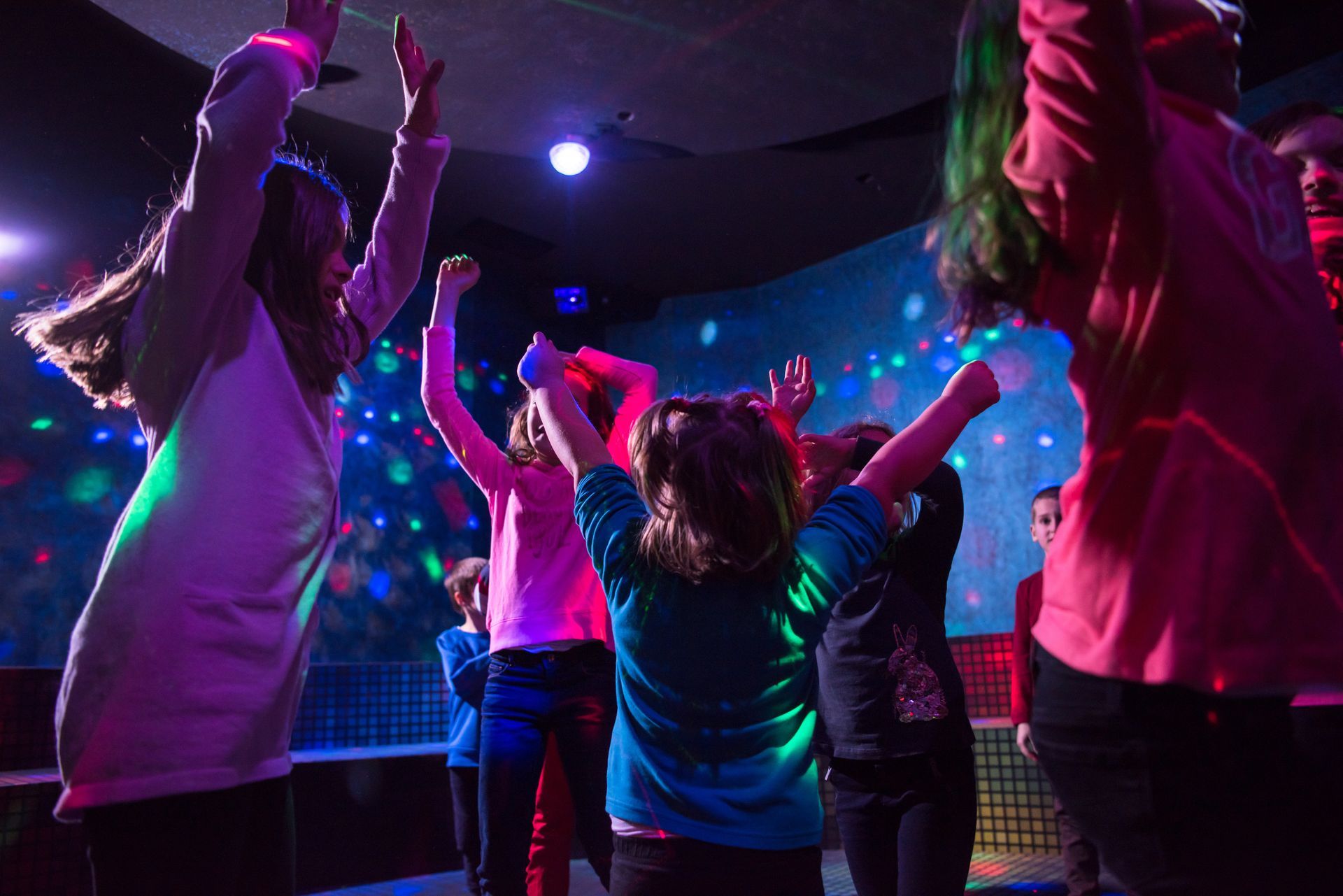 Group of children jumping and dancing on a lit stage with colorful disco lights in the background.