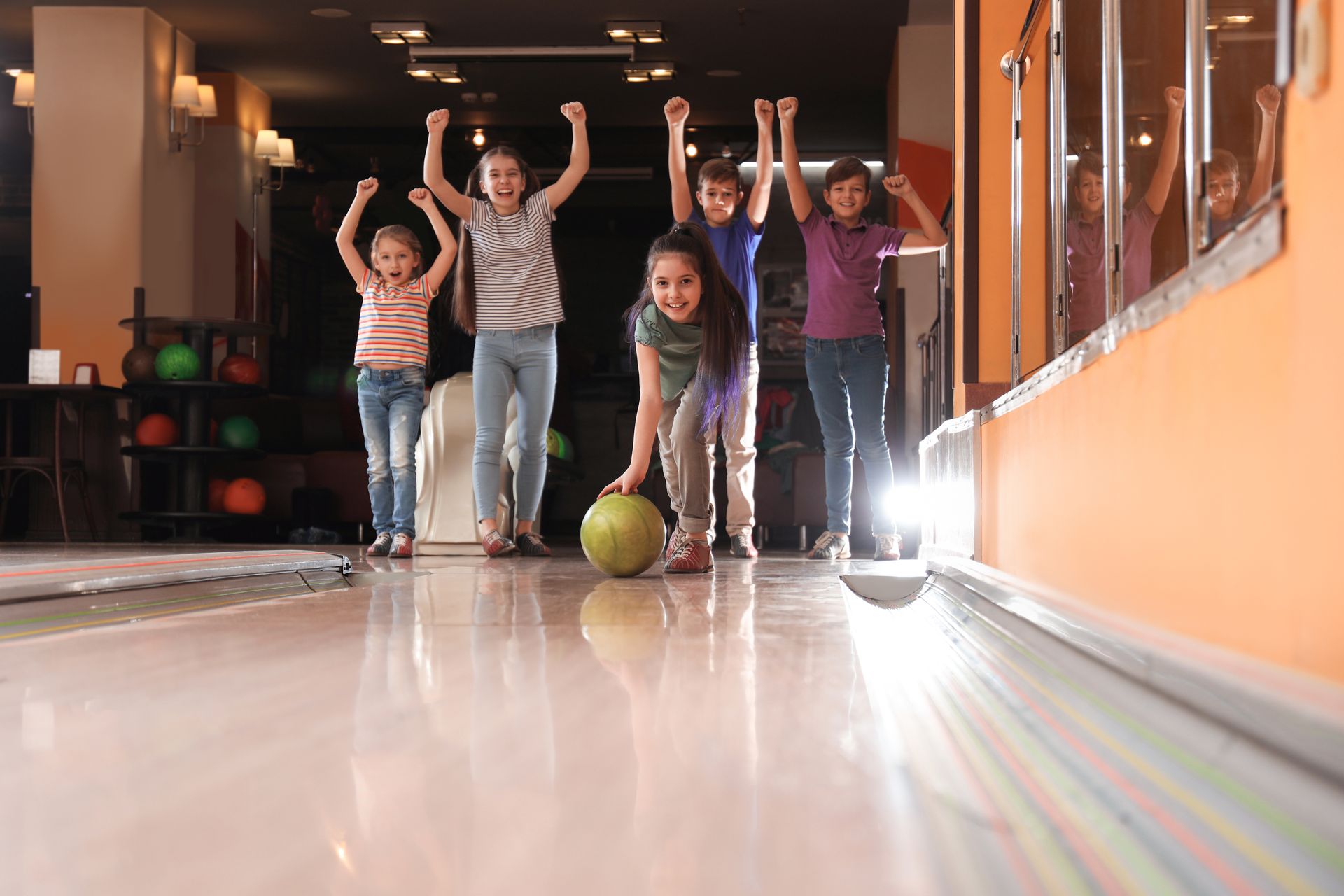 Girl throwing a bowling ball and enjoying time with friends.