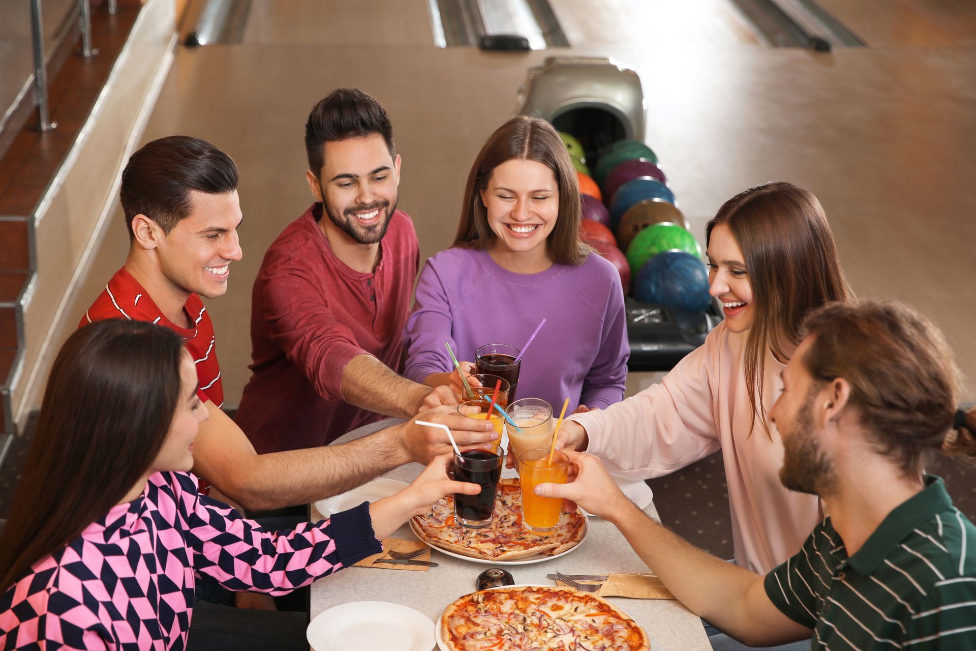 Friends enjoying drinks and pizza together at a bowling alley. Friends enjoying drinks and pizza together at a bowling alley.