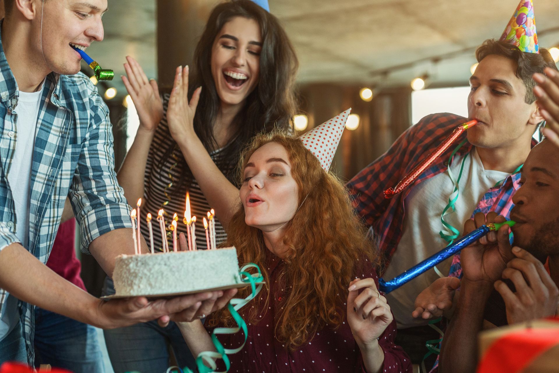 A person blowing out candles on a cake with a group of people around | Birthday Celebration Parties