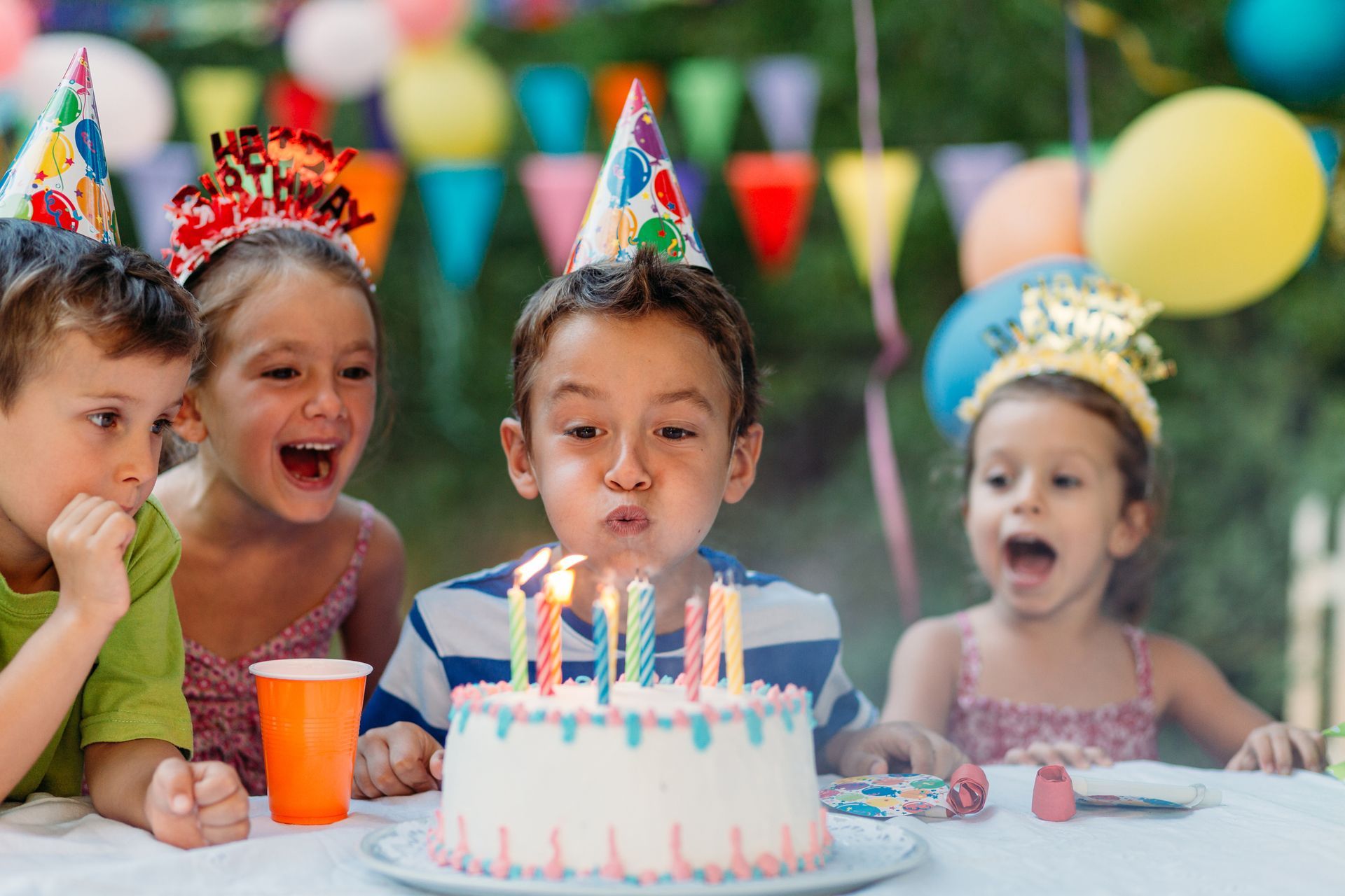 A kid is blowing a candle surrounded by other kids. A kid is blowing a candle surrounded by other kids.