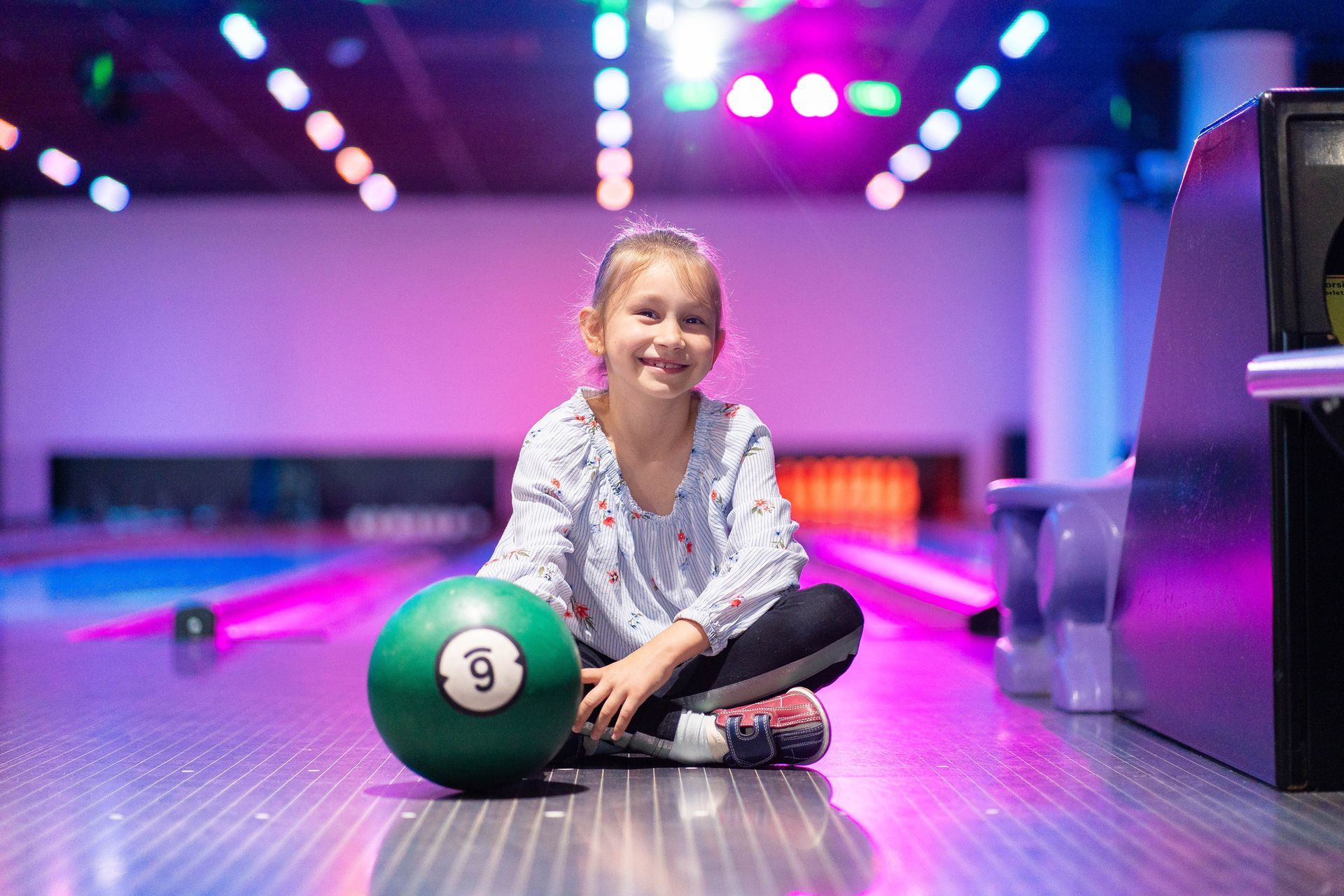 Smiling young girl seated on the lane at a bright bowling alley. Smiling young girl seated on the lane at a bright bowling alley.
