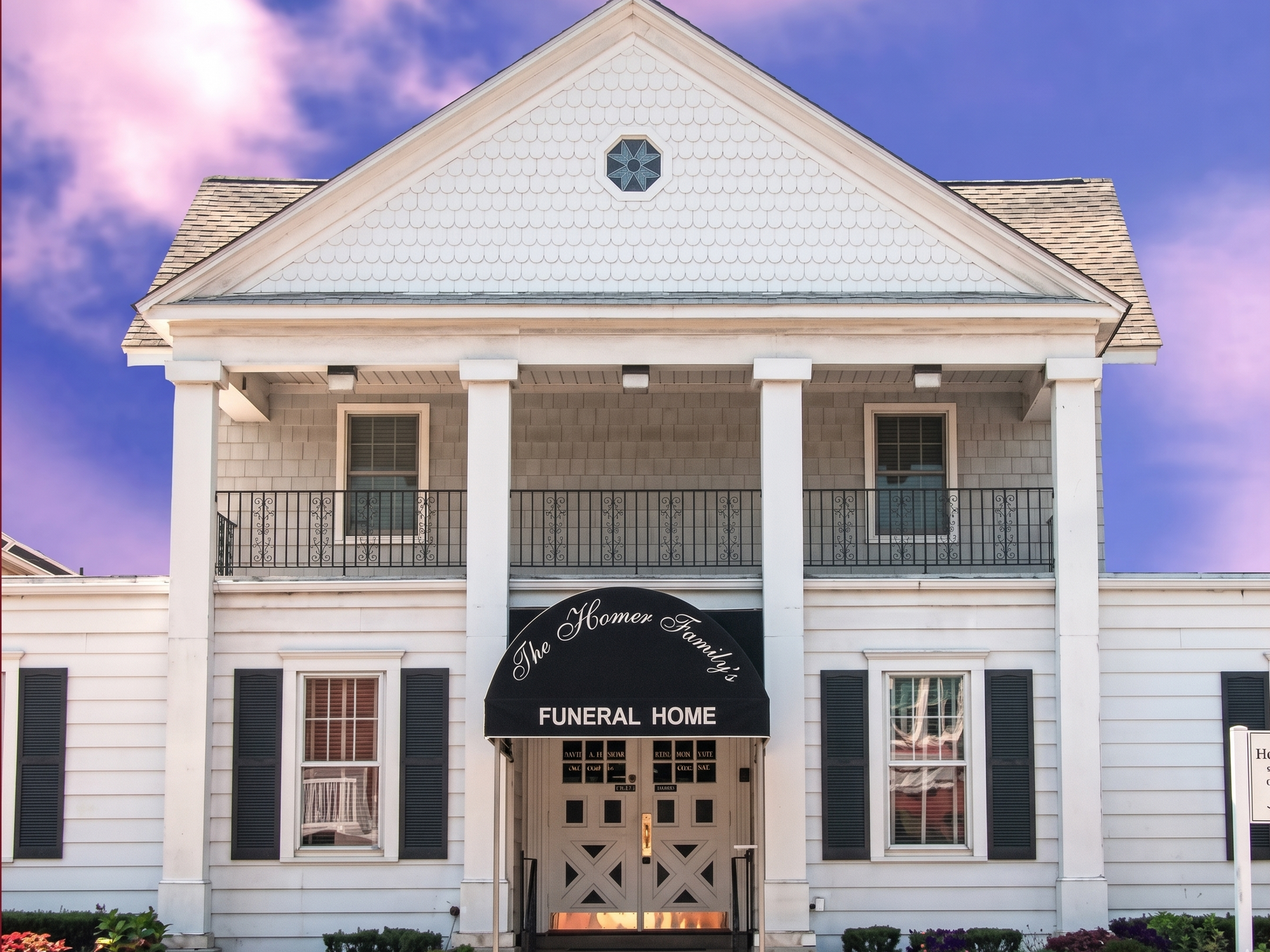 White funeral home building with columns, black awning, and pink-purple sky above.