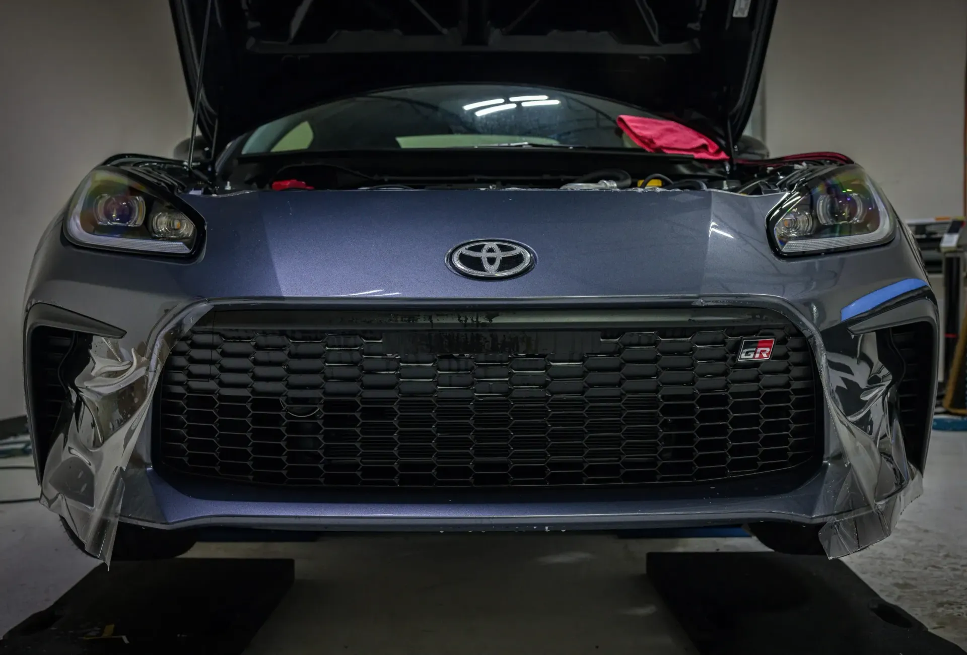 Dark gray Toyota GR86 with the hood open, parked indoors.