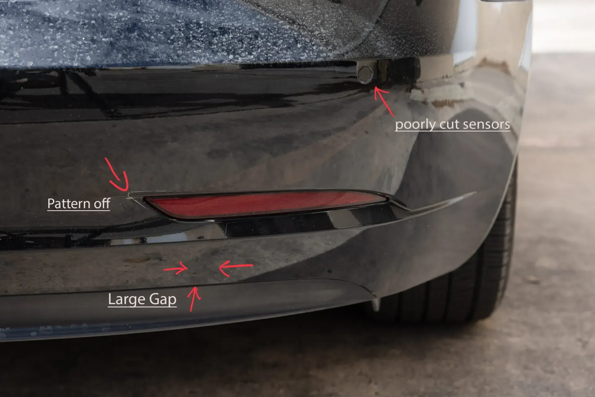 Close-up of a damaged black car bumper with large gap, paint chip, and parking sensor.