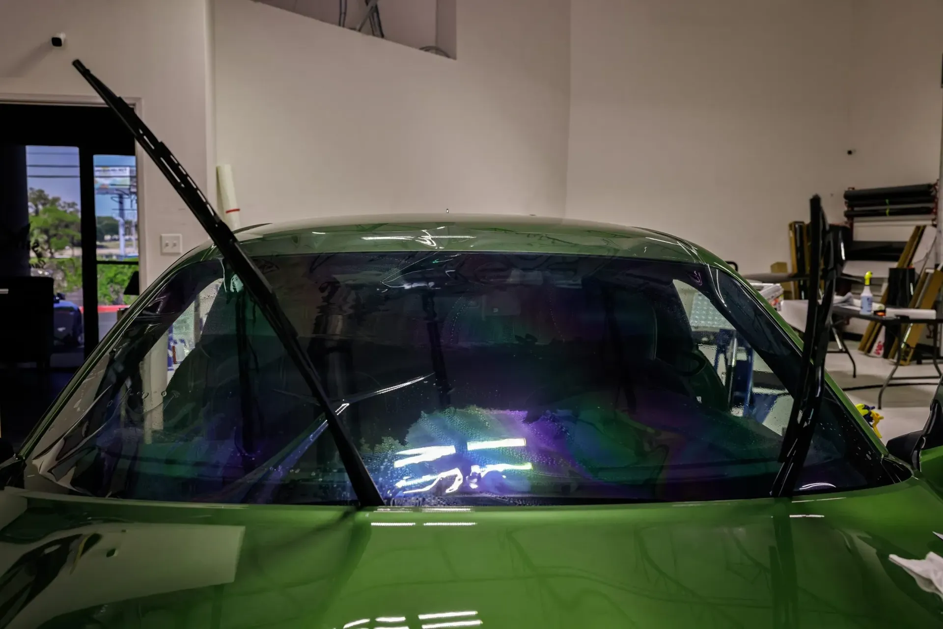 Green car windshield with iridescent film, wipers raised.
