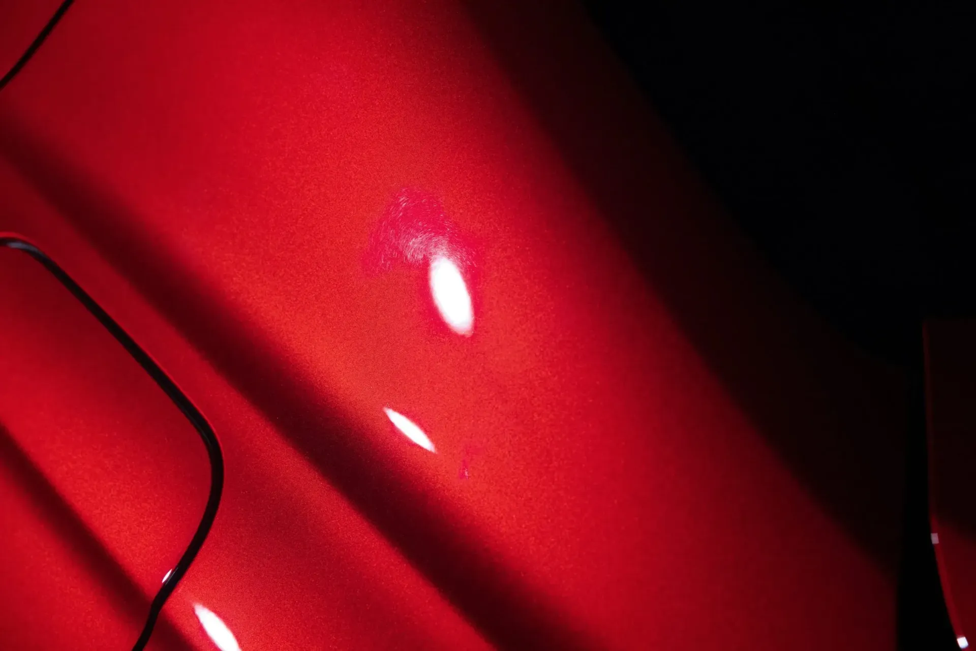 Red car paint, with a bright white spot and reflections.