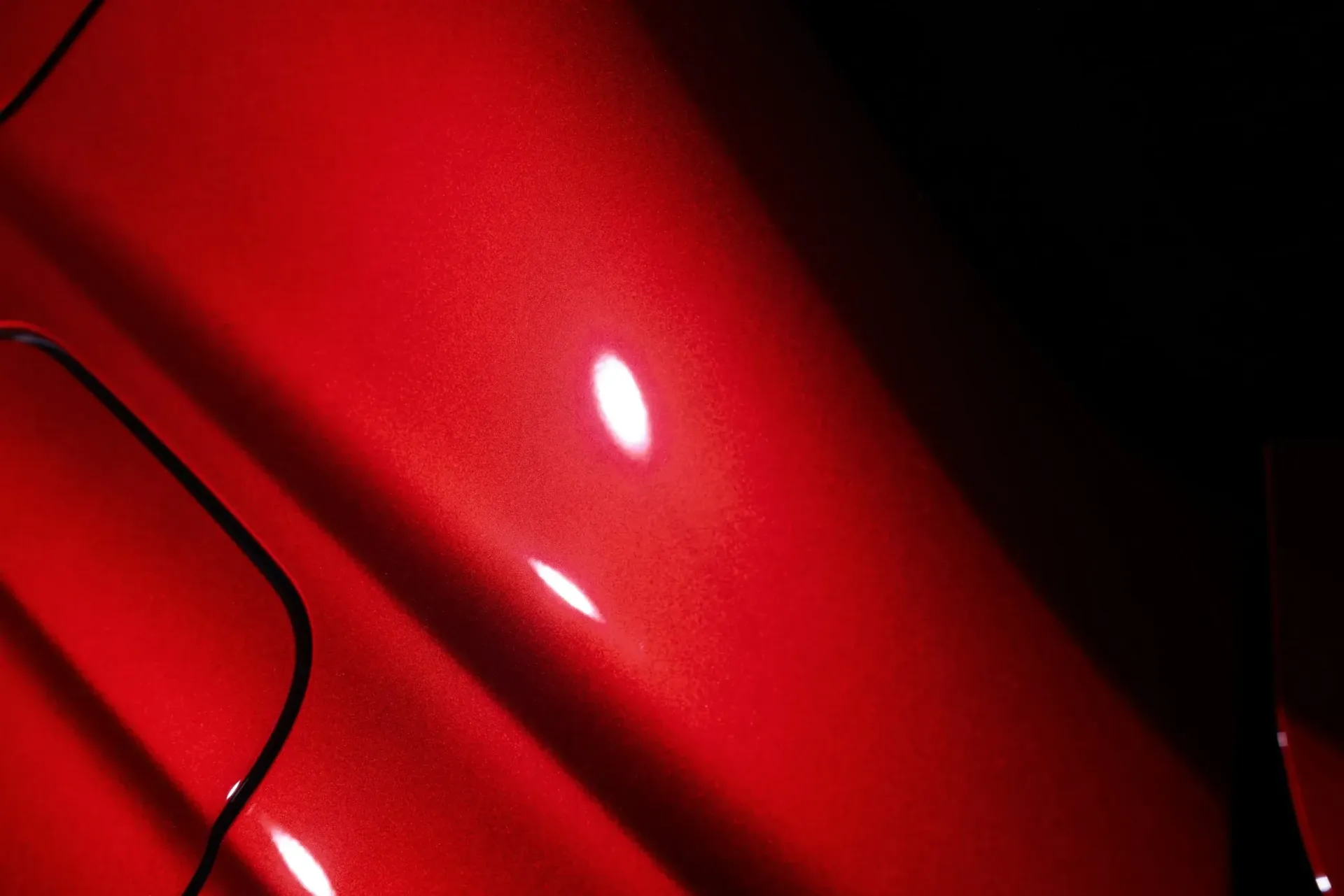 Close-up of red car paint with bright reflections and dark shadows.