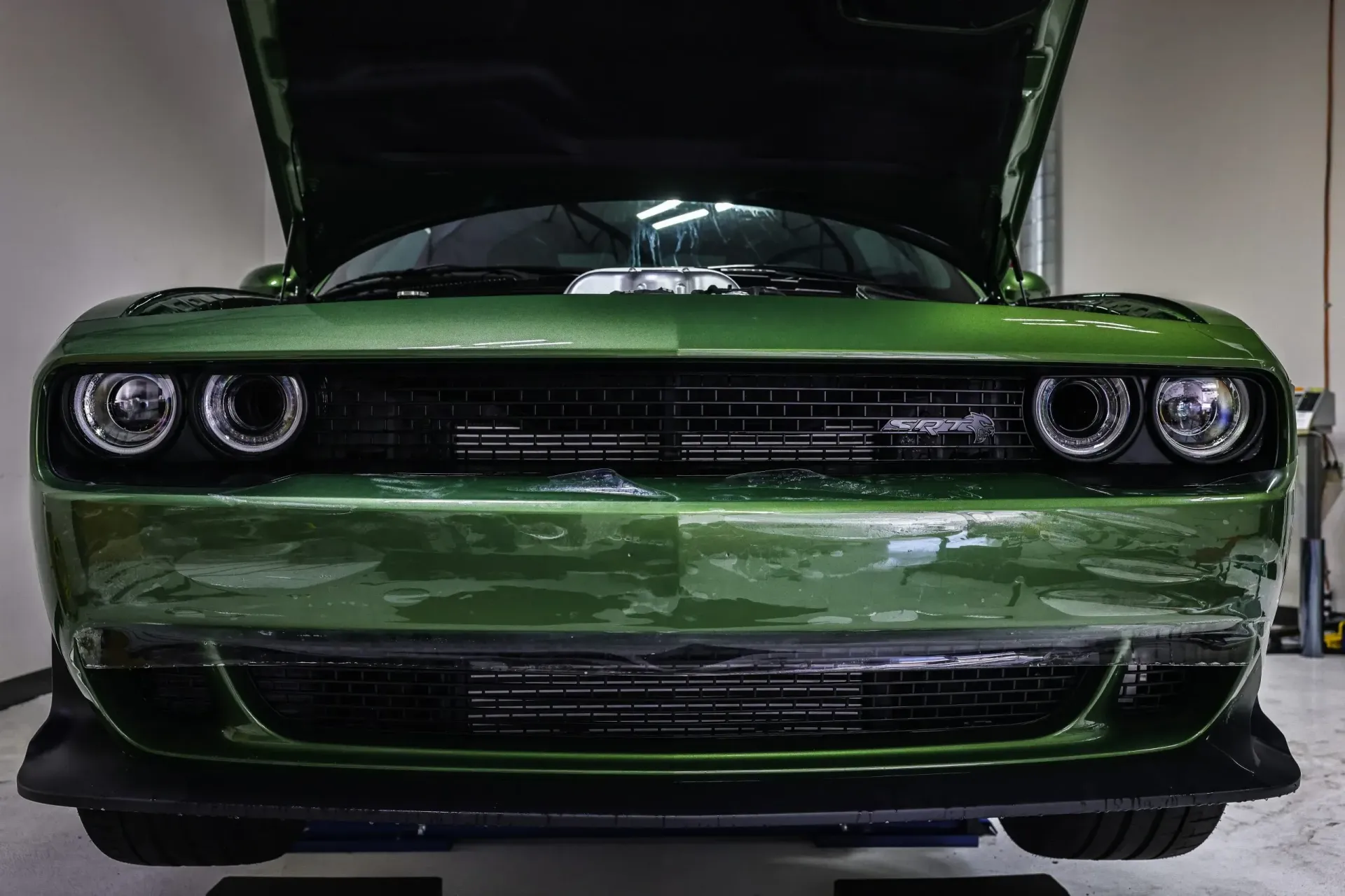 Green Dodge Challenger with hood up, revealing the engine in a garage.