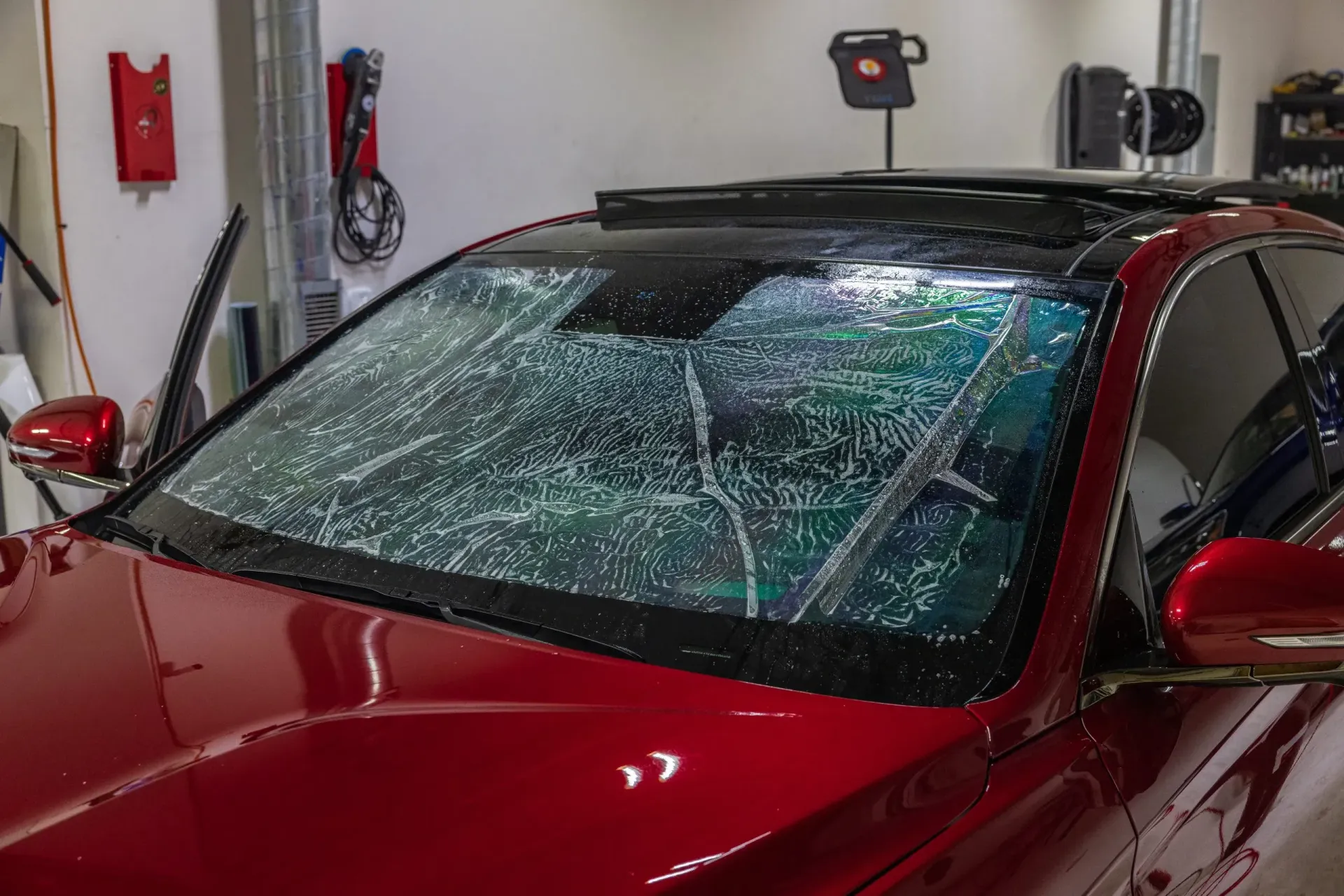 Red car with soapy windshield being cleaned inside a shop.