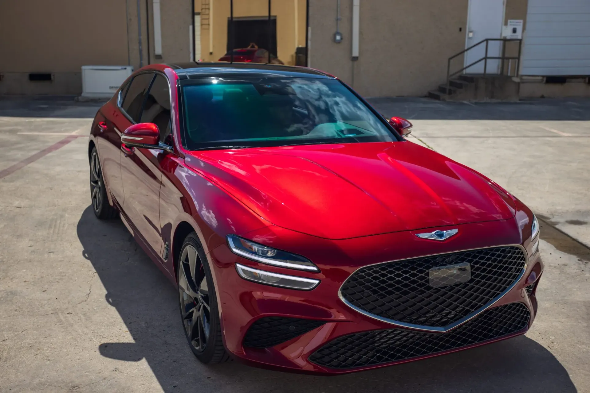 Red Genesis G70 sedan parked in front of a building on a sunny day.
