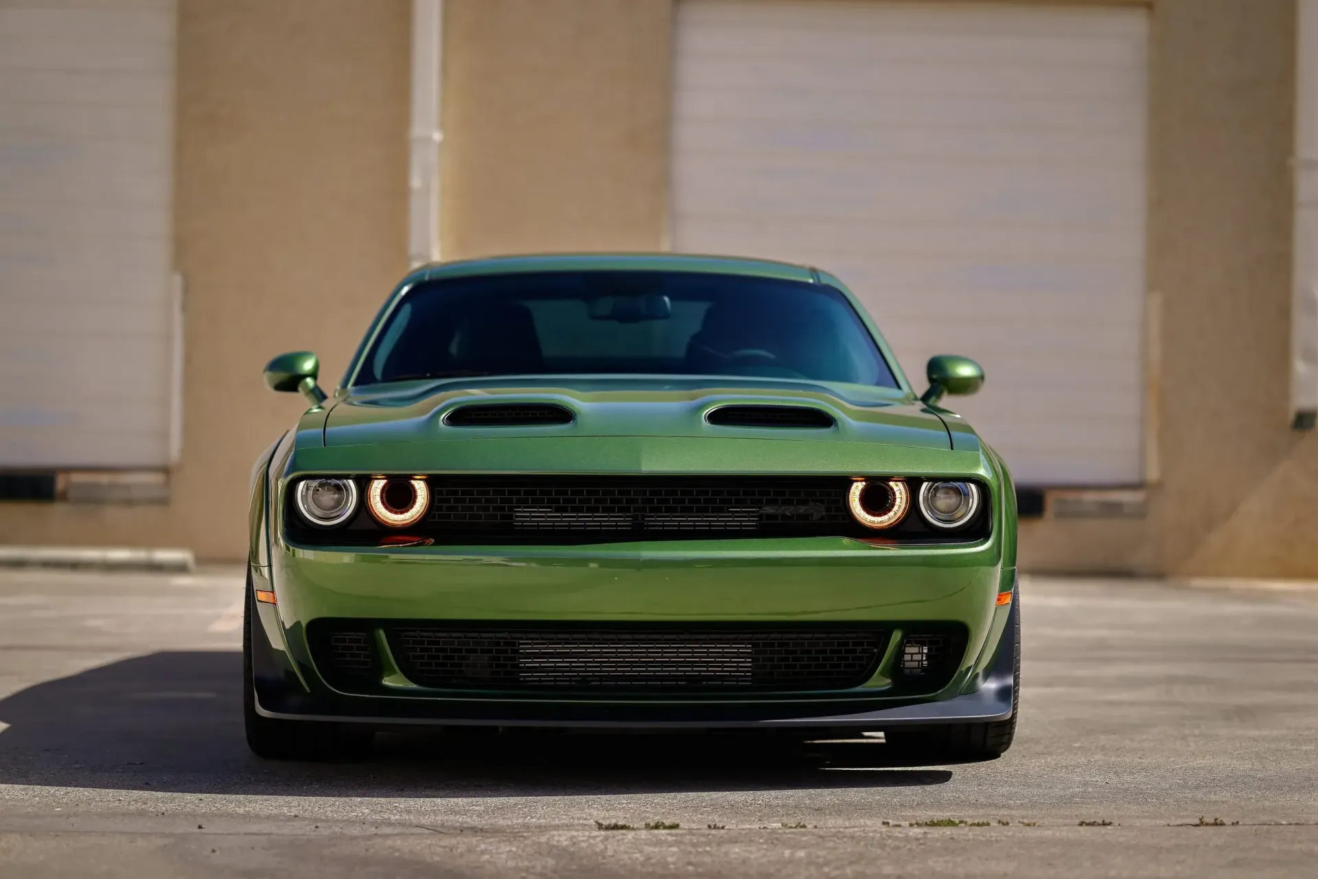 Green Dodge Challenger, front view, parked in front of a building with a garage door.