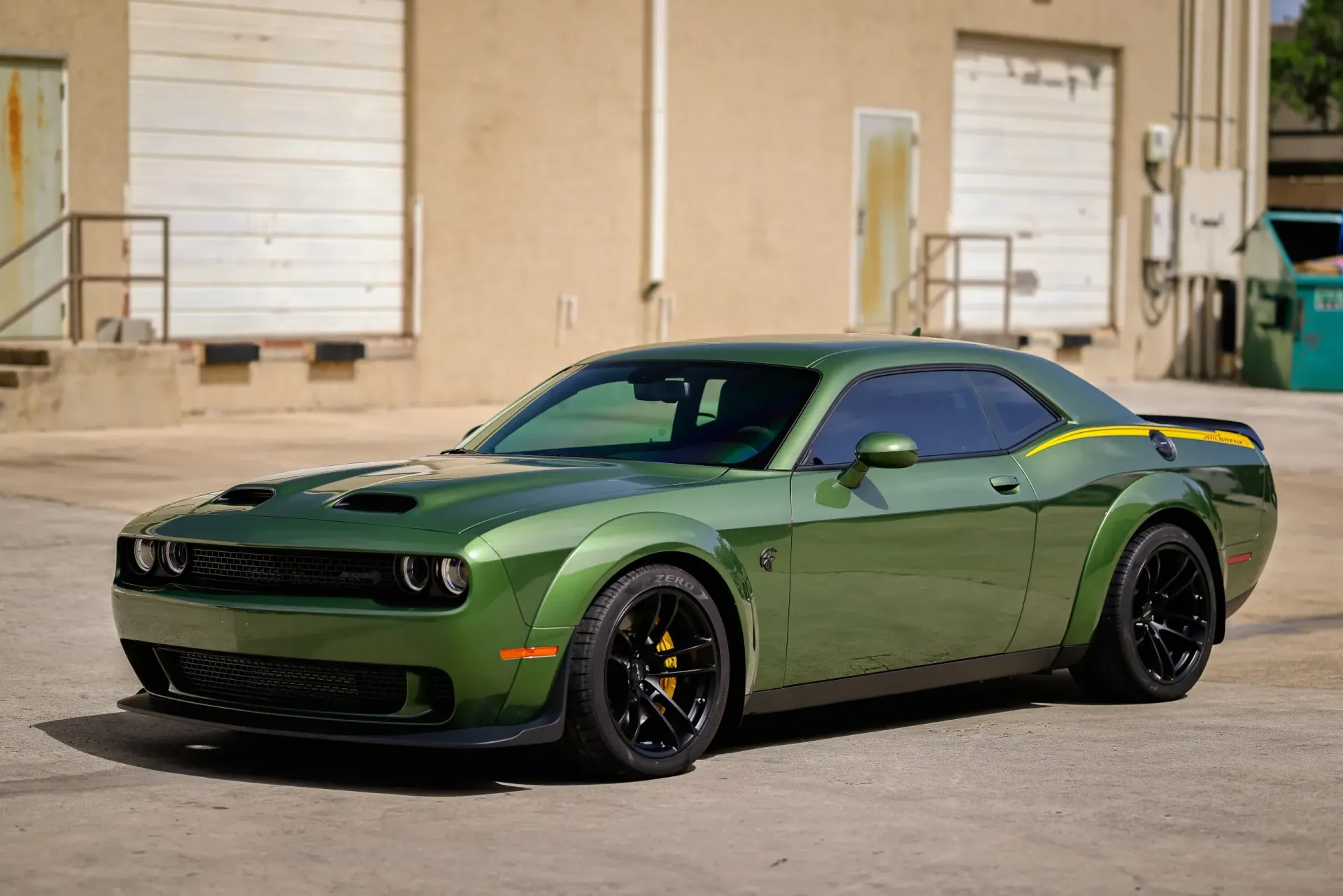Green Dodge Challenger parked outside building. Black wheels, yellow accent stripe.