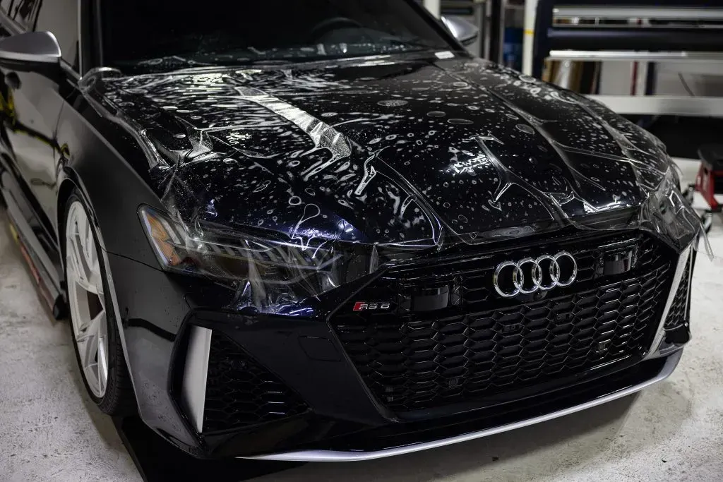 Black Audi car with protective film applied to the hood in a garage.