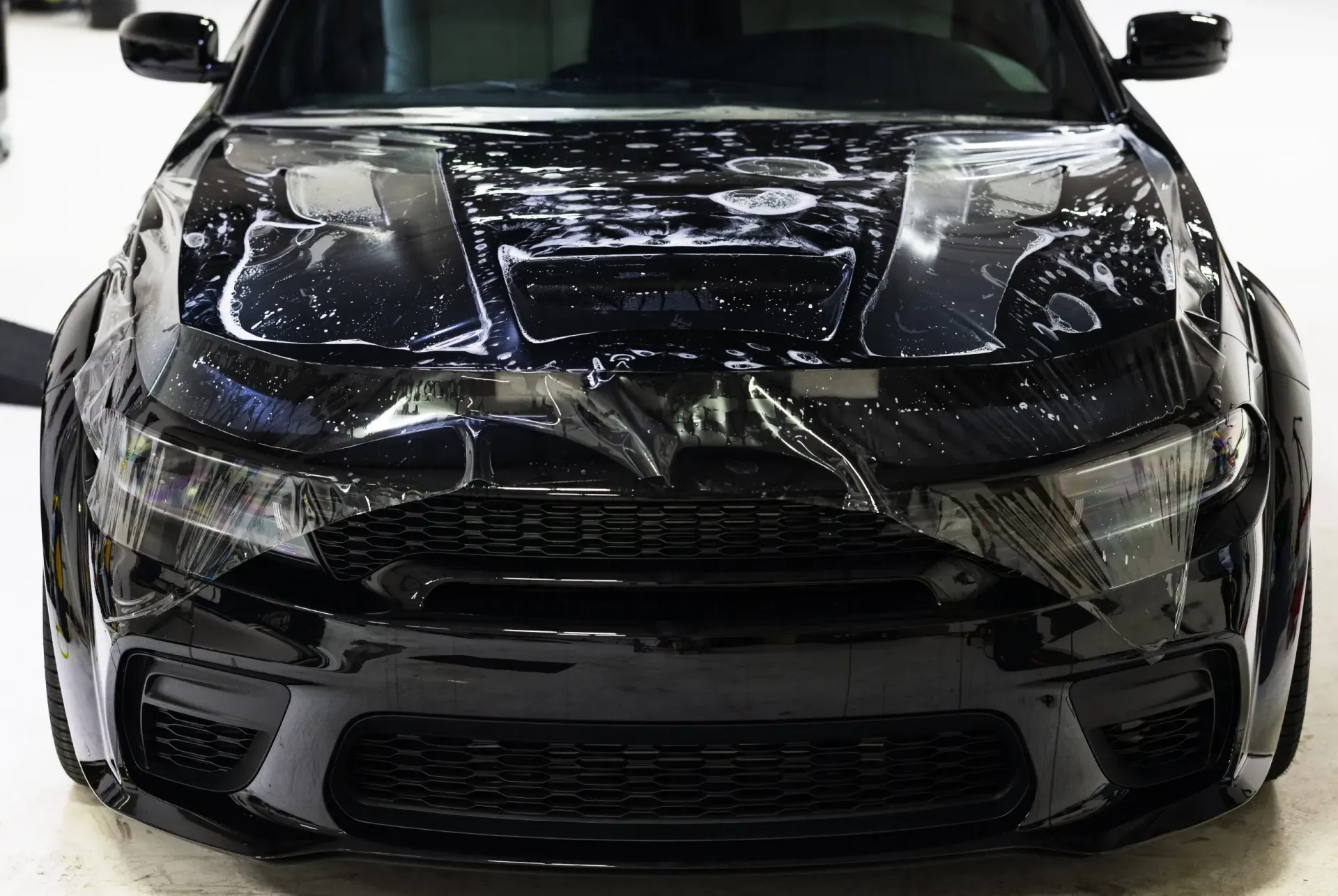 Black car front, covered with protective film, in a showroom.
