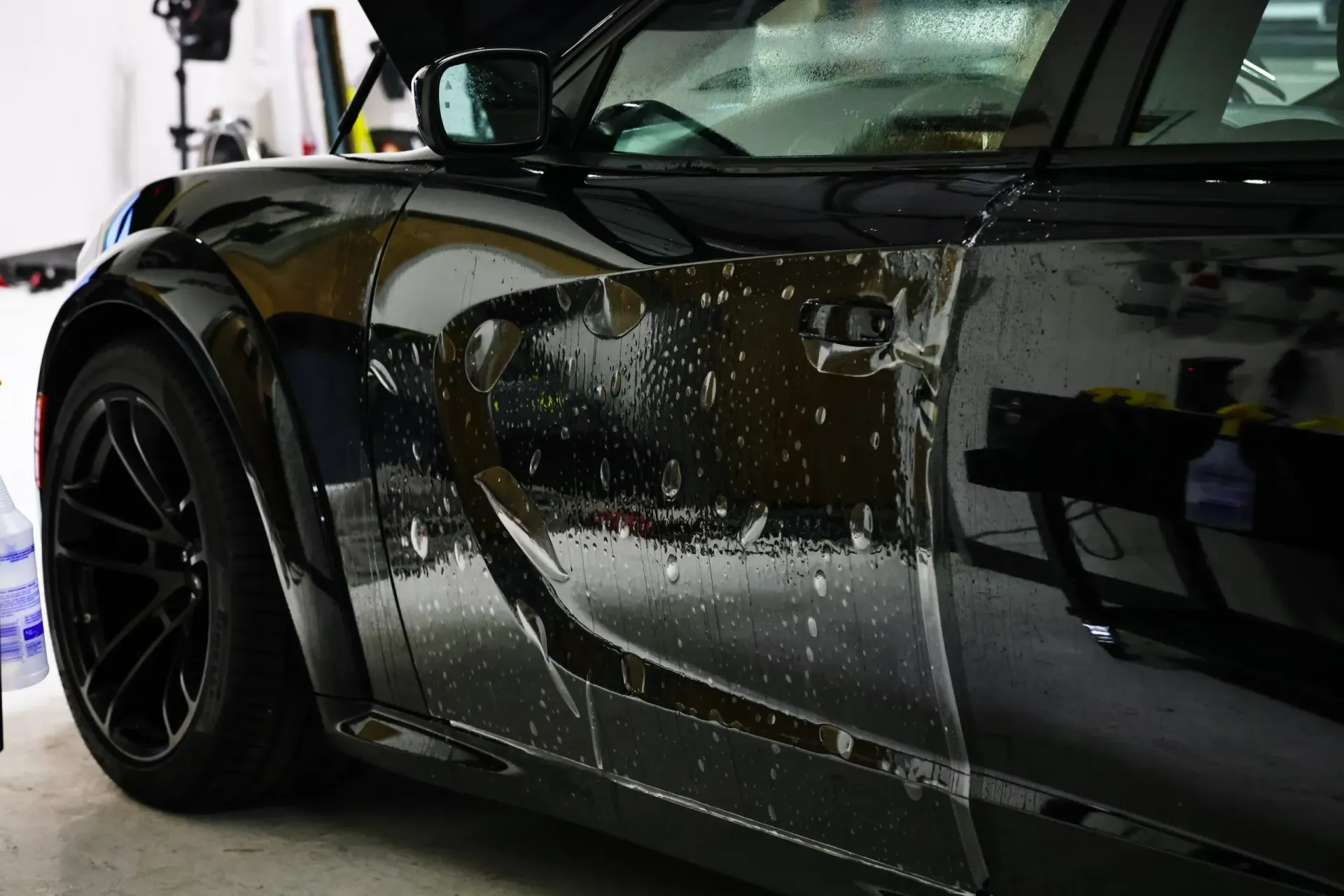 Black car door covered in wet film; detail from front quarter panel.