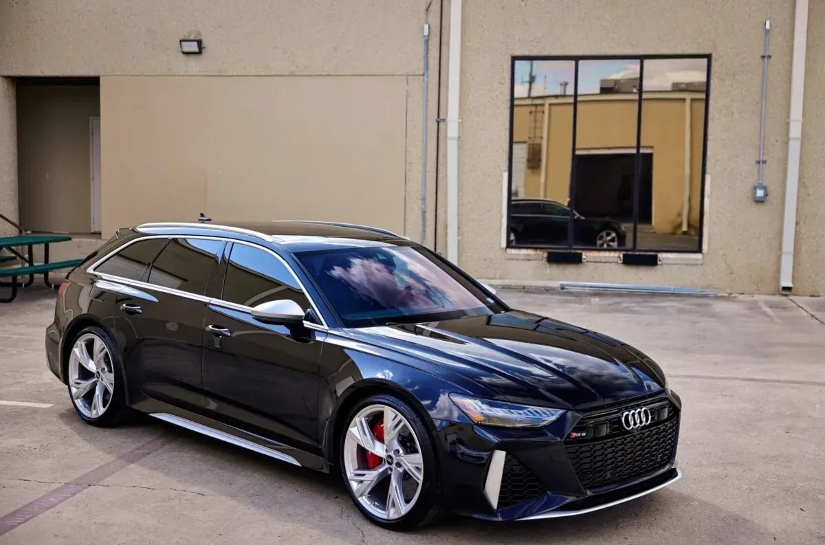 Black Audi RS6 Avant parked in front of a building with a large window.