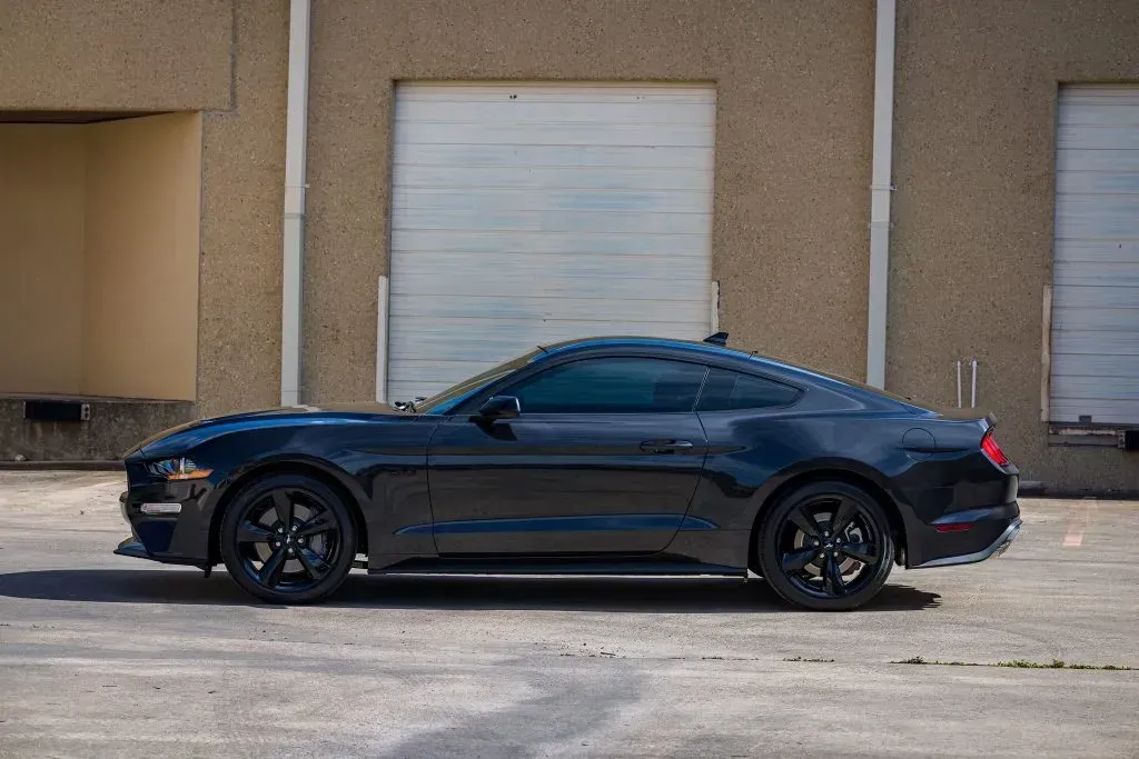 Black Ford Mustang parked in front of a tan building with closed garage doors.