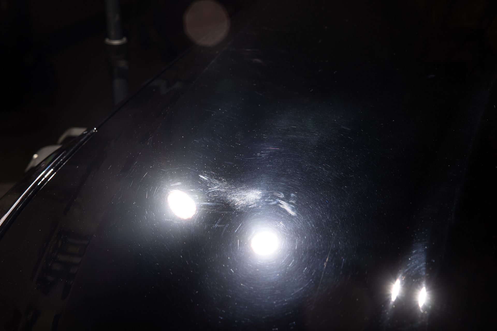 Black car hood with scratches, reflecting bright lights.