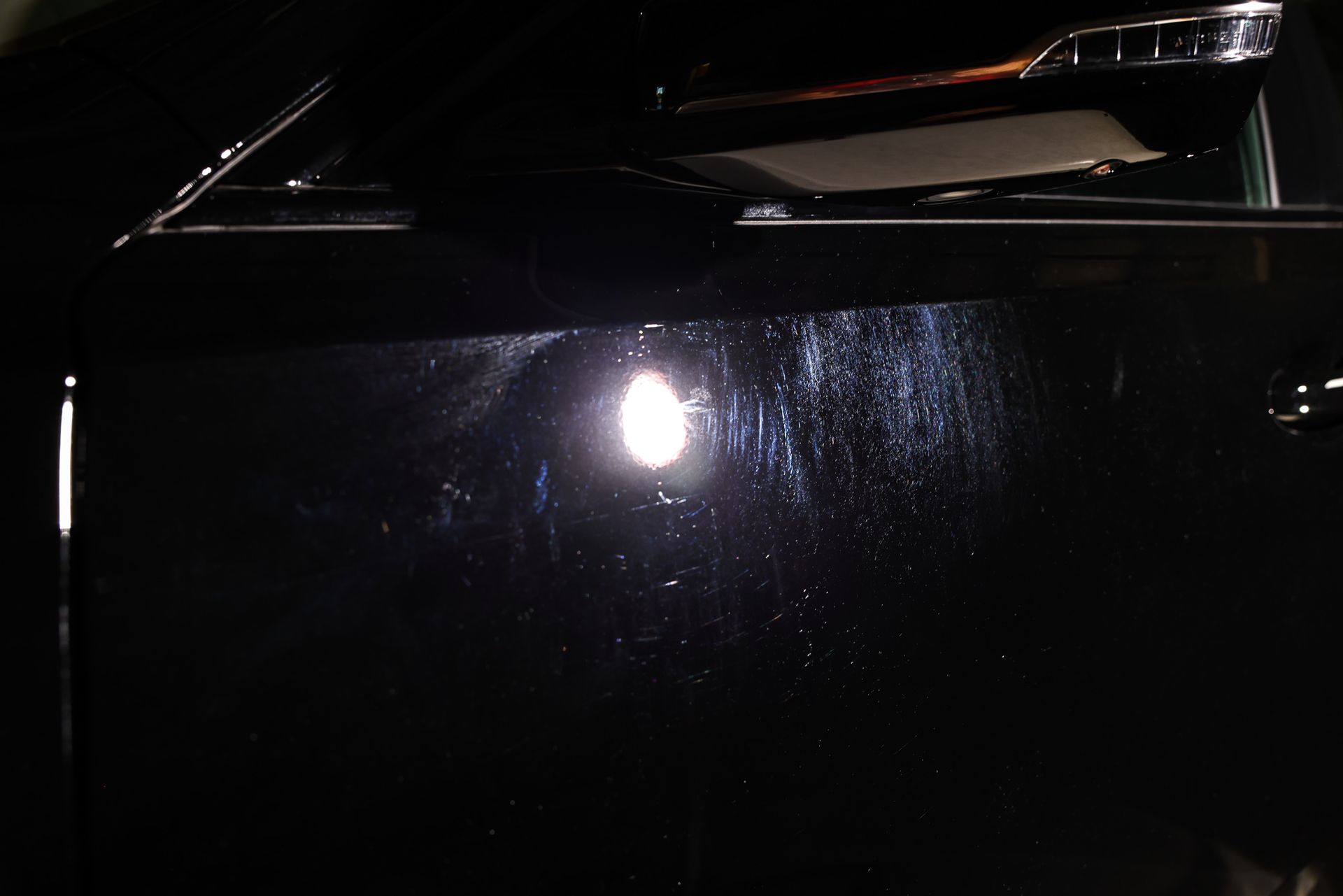 Black car door with light reflection and scratches. Chrome side mirror visible.
