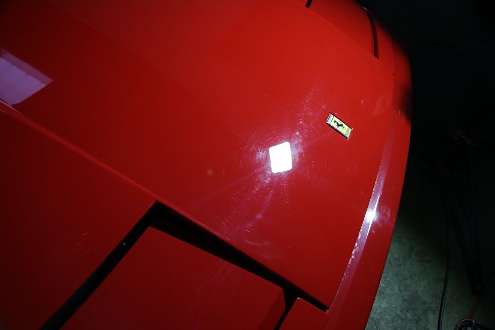 Red car hood with Ferrari emblem reflecting light.