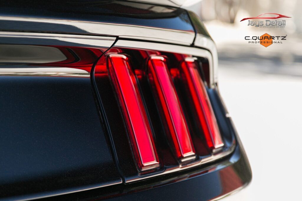 Red taillights on the black rear of a Ford Mustang.