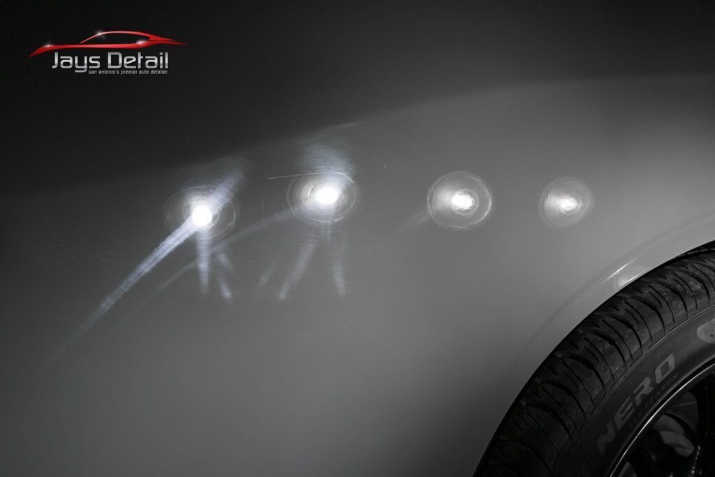 A car's gray fender with reflections showing scratches; a tire is visible on the right.
